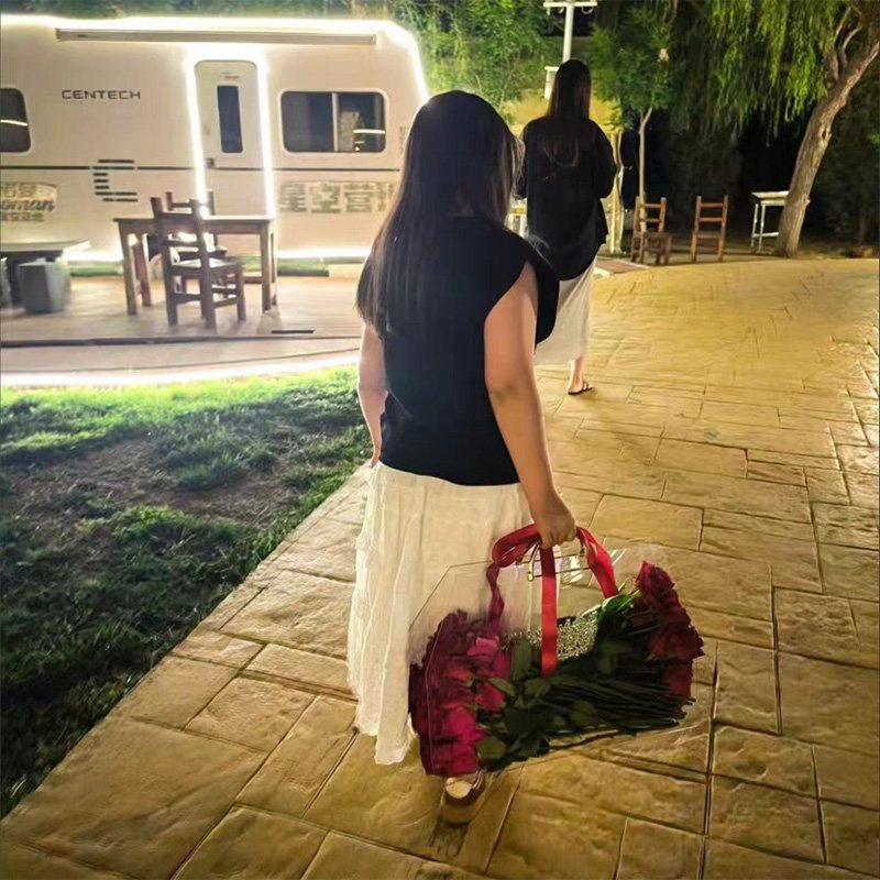 Woman carrying transparent acrylic flower bag with red handles filled with red roses at night